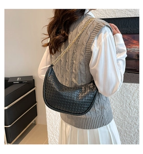 Detail of a black woven crescent hobo bag with gold chain strap on a female model