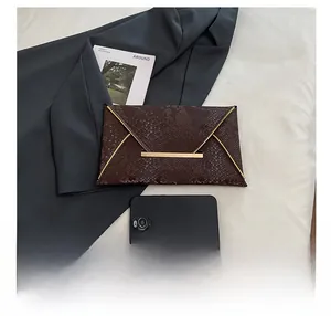 Pochette marron à motif serpent et cadre doré, présentée avec un smartphone pour la taille