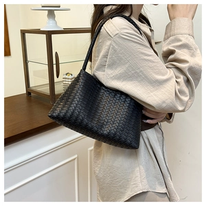 Detail of black woven leather texture and rectangular silhouette on women's shoulder bag