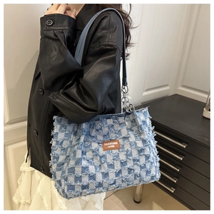 Detail of blue and white checkered denim tote with fringe edges and brown leather tag