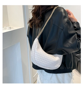 Detail of white woven texture crescent bag with gold chain strap on shoulder