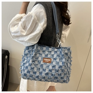 Detail of blue and white checkered tote bag with frayed edges and brown leather patch