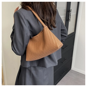 Detail of a brown woven leather shoulder bag styled on a model in a minimalist setting