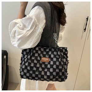 Detail view of black and gray checkered tweed tote bag with leather logo and chain strap