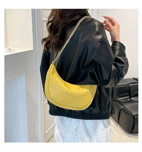 Detail of yellow woven hobo bag with gold metal chain strap worn on a black leather jacket