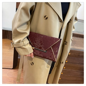 Détail de la pochette enveloppe rouge vin foncé avec motif serpent et boucles dorées
