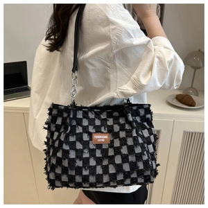 Detail of checkered tote bag with fringe edges, leather strap and metal chain links