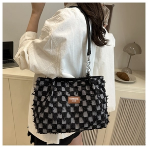 Detail of checkered tote bag with frayed edges and brown leather brand label on side