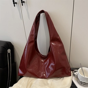 Minimalist deep red hobo shoulder bag with glossy patent leather finish in a lifestyle setting