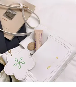Detail of white PU leather bucket bag with floral charm and practical front slot pocket