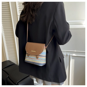 Detail of colorful striped straw bag with brown leather flap and metal logo