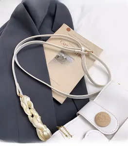 Close-up of white bucket bag featuring wooden decorative buckle and silk shoulder strap detail