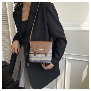 Detail of colorful striped woven straw crossbody bag with brown leather flap and metal logo