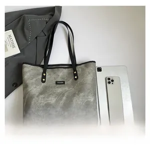 Vista piatta di una borsa tote grigia con manici neri e dettagli con rivetti