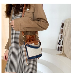 Close-up of canvas bucket bag with navy leather trim and elegant gold hardware detail