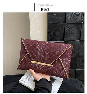 Détail d'une pochette enveloppe rouge avec texture peau de serpent et bords métalliques dorés