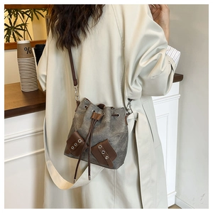 Detail view of canvas and brown leather bucket bag with drawstring on a model