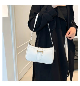 Moderne weiße Leder-Sichel-Schultertasche mit goldener Metallschnalle über einem schwarzen Mantel
