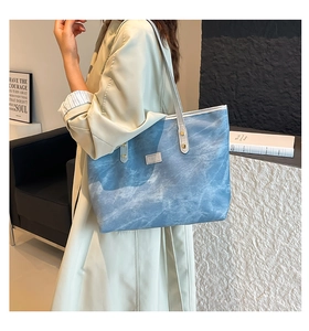Dettaglio della borsa tote azzurra con trama marmorea e rivetti dorati indossata da modella