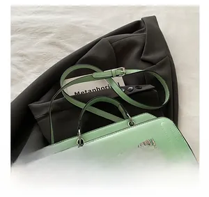 Detail shot of a gradient green crossbody bag featuring polished leather and metal logo