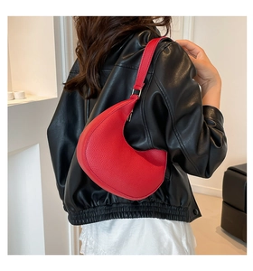 Detail view of red lychee grain leather crescent bag worn by a model in black leather jacket