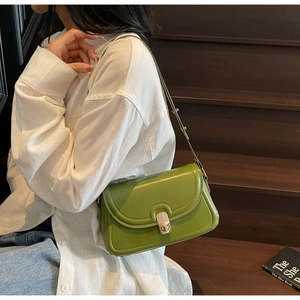 Detail of green leather crossbody bag with golden buckle on a model in sunlight