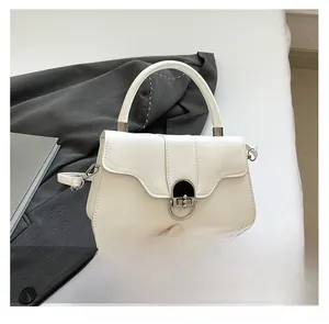 Detail view of the silver metal clasp and smooth cream faux leather of the shoulder bag