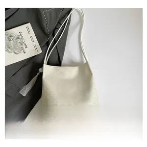 Detail view of cream-colored leather tote bag with logo embossing and tassel charm