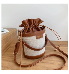 Detail of retro bucket bag with cream fabric, brown leather trim and gold drawstring hardware