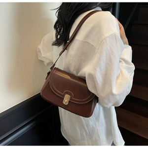 Detail of dark brown leather crossbody bag with a gold rectangular metal lock closure