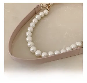 Close-up of pink leather handbag strap with large imitation pearls and gold metal hooks