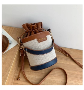 Close-up of canvas bucket bag with leather trim and drawstring on wooden table