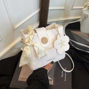 Sac seau en cuir blanc avec boucle en bois et foulard en soie sur un fond de livre