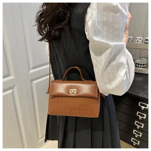 Close-up of brown leather bag featuring geometric embossing and golden twist-lock closure