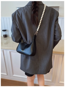 Detail of black crescent shoulder bag with large pearl strap worn over a grey blazer