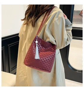 Detail view of burgundy bucket bag featuring textured pattern and pearl tassel charm