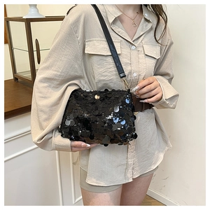 Detail of black sequin shoulder bag with golden metal hooks worn by a model in interior