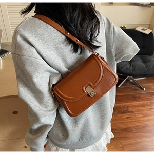 Caramel brown leather crossbody bag with silver twist lock shown in a casual lifestyle setting