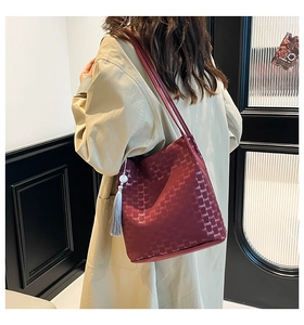 Detail view of large burgundy tote bag with logo pattern and grey tassel charm