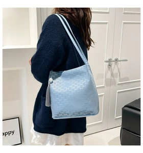 Detail of light blue bucket bag with letter logo print and fringe tassel on model
