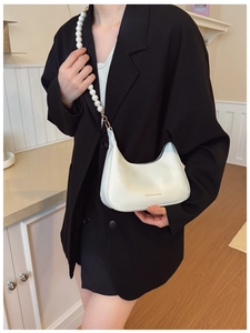 Detail of white half-moon bag with large pearl strap over a black suit