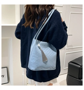 Detail of light blue monogram shoulder bag with tassel and pearl charm on a model