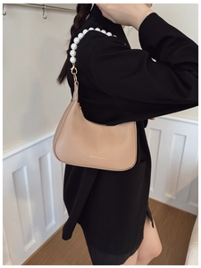 Detail of beige crescent underarm bag featuring a stylish oversized white pearl strap handle