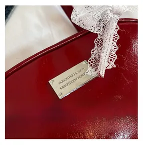 Dettaglio borsa in pelle verniciata rossa con targa logo argento e fiocco di pizzo