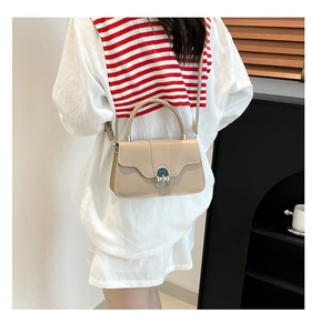 Detail view of beige crossbody bag featuring a round metal buckle with green stone inlay