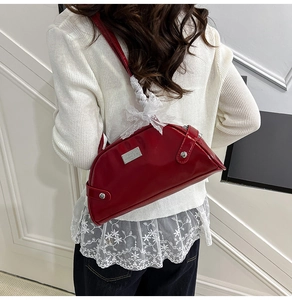 Dettaglio borsa a spalla in pelle verniciata rossa con fiocco in pizzo bianco e placca