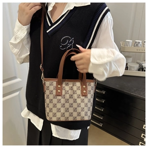 Detail of retro checkered tote bag with brown leather trim and metal rivet accents