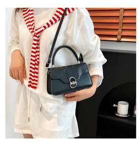 Detail view of the silver oval metal lock and smooth black leather on a chic crossbody bag
