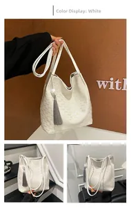 Detail view of white monogram tote bag with embossed textures and tassel pendant