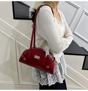 Dettaglio di una borsa sottobraccio bordeaux in finta pelle liscia con logo metallico